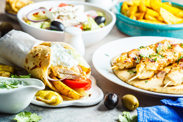 Greek food: salad, chicken souvlaki, gyros and baked potatoes on gray background. Traditional greek cuisine concept.