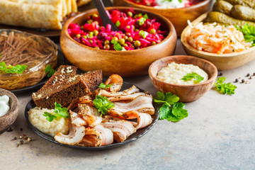 Traditional Russian cuisine concept. Borsch, jellied meat, lard, crepes, salad vinaigrette and sauerkraut, gray background.