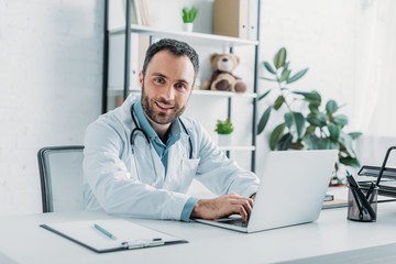 smiling doctor looking at camera while using laptop