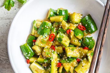 Asian smashed cucumber salad with chili and sesame seeds in white bowl, top view. Chinese food concept.