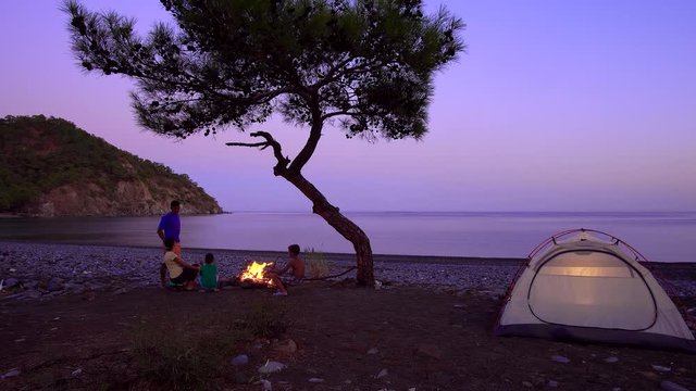 Beautiful evening view of the sea bay, tents and tourist family near the campfire. Freedom and travel concept. 4K