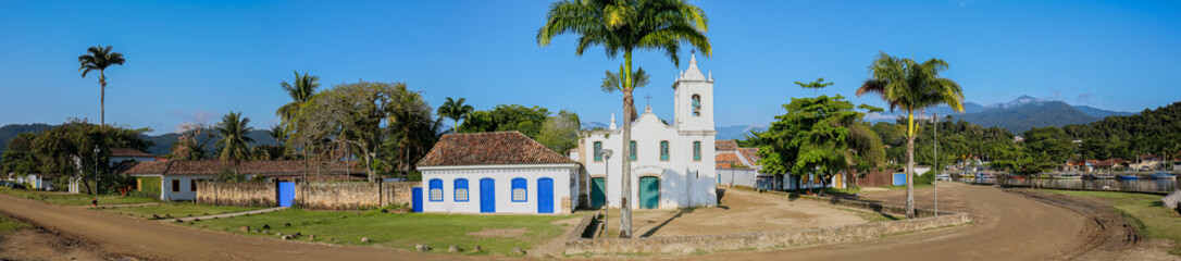 Fototapeta na wymiar Arial view panorama of church Nossa Senhora das Dores (Our Lady of Sorrows) with palm trees and green mountains in background on a sunny day, historic town Paraty, Brazil