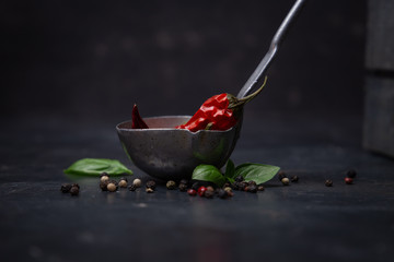 Chili pepper with basil and peppercorns in a ladle on a rustic surface,