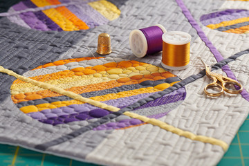 Sewing accessories lying on a mini quilt with orange-purple geometric pattern