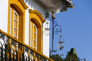 Fototapeta na wymiar Close up of an artful colonial house corner with two yellow framed high glass doors, metall balustrade and a lantern in sunshine, historic town Paraty, Brazil