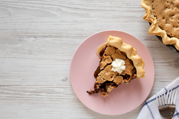 A slice of homemade Chocolate Walnut Derby Pie on a pink plate on a white wooden surface, top view. Overhead, from above, flat lay. Copy space.