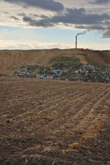 Empty farm field with garbage, waste dump and chimney at background