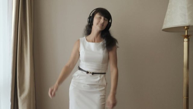 Happy Young Woman Dancing And Have Fun In Room Listening To Music On Wireless Headphones. Business Woman Enjoying Dance, Having Fun Party. Floss Dance Viral, Flossing. Technology. Slow Motion. .