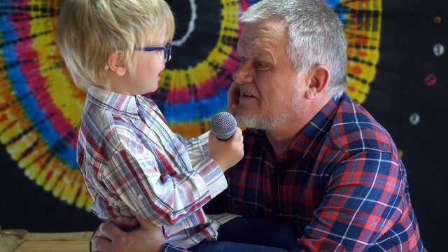 blond child and father with gray hair and beard in plaid shirts celebrate family holiday together. Father sings karaoke,  boy holds microphone. Lovely family duet