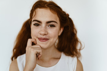 a mischievous girl tries to keep a smile while holding her finger on her chin, luxurious hair is gathered in ponytails. gray background