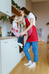 little daughter holds her mother by the cheeks, sitting on the countertop in the kitchen and gently looks at her - 309912849