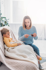 attentive mother pouring cough syrup in spoon while sitting near sick son