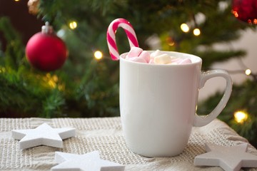 Obraz na płótnie Canvas Cup of coffee with candy cane in front of Christmas tree