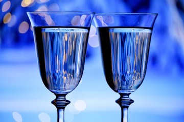 Two glasses with champagne sparkling wine on a festive blue background with lights and bokeh. The atmosphere of celebration and happiness.
