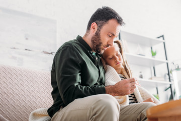 upset man looking at thermometer while hugging diseased daughter