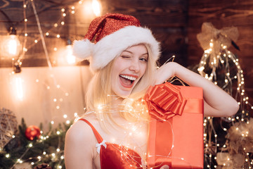 Christmas winking girl posing with red gift box, wink at camera. Woman with a big present in her hands. Smile. Hapiness. Christmas time.