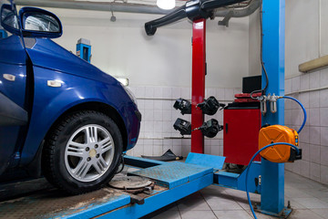 Blue car front wheel view stands on the stand wheel alignment convergence of the car during regular maintenance in the workshop for repair of vehicles . Auto service industry.