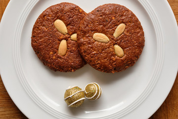 Still life with a  pair of delicious brown Elisengingerbreads with almonds and christmas decoration lying on a pure white porcelain plate on a wooden table