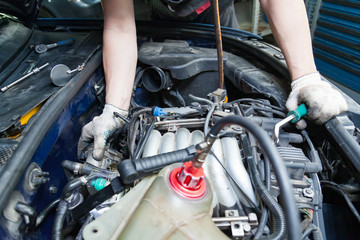 A car repairman unscrews parts with a wrench with a green handle in the engine compartment suh as spark plugs and ignition coils in a vehicle repair workshop. Auto service industry.