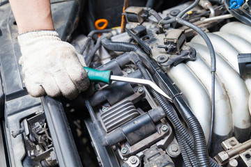 A car repairman unscrews parts with a wrench with a green handle in the engine compartment suh as spark plugs and ignition coils in a vehicle repair workshop. Auto service industry.