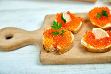 Salmon red caviar in bowl and Sandwiches with on wooden cutting board on white background copy space.