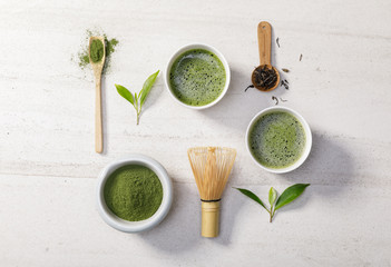 Organic matcha green tea powder in bowl with wire whisk and green tea leaf on white stone table,...