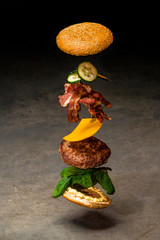 Flying cheeseburger ingredients on dark background of concrete. Fastfood concept. Ingredients of...