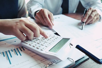 Businessman analyzing investment charts and pressing calculator buttons over documents. Accounting Concept.