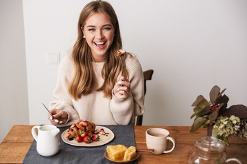 Obraz na płótnie Canvas Image of happy caucasian woman eating croissant while having breakfast