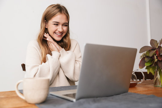 Image of excited young woman using laptop and drinking tea