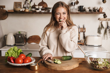 Image of pleased cute woman winking and eating cucumber