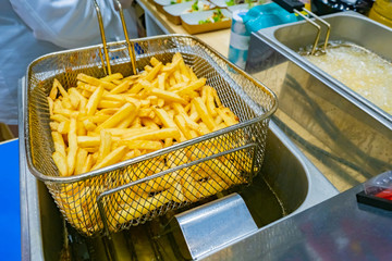 French fries. Work with a deep fryer. Hot oil. Oil drains from potatoes. Cooking french fries. Work in a restaurant. Fast food restaurant. Concept - harmful food. Snack. Cafe. Crispy potato