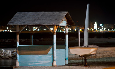 wooden cabin sand rocks beach, boat  and city lights in the background