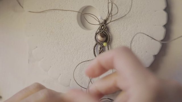 Lifestyle concept, work from home to reinvent your life: close-up detail of woman hands making macrame knotted jewel with some colored thread spools in foreground and bokeh effect filmed in flat color