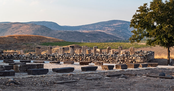 ruins of an israelite stone storehouse made with pillars and columns at the tel hazor archaeological park in israel with the canaanite city and kibbutz ayelet shahar in the background