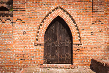 Wooden door of an exposed brick church. Ozzano Monferrato