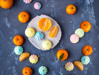 Tangerines and multi-colored Bizet cookies on a gray background and a wooden spiel