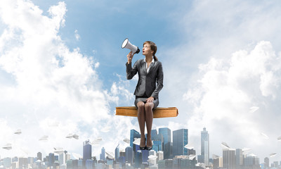 Young woman with megaphone sitting on big book