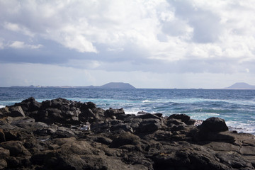 Fototapeta na wymiar Deep blue water with waves, white foam and volcanic rocks