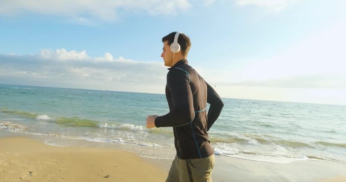 Fit male runner training on the summer beach and listen to music against beautidul sky and sea , UHD 4K