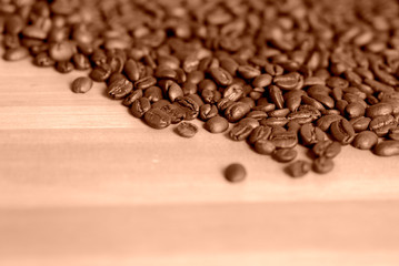 Roasted coffee beans scattered on a wooden surface close-up. Food background brown color toned