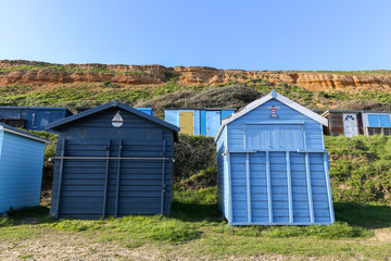 Blue beach huts in front of a sandy cliff in Hampshire, south of England.