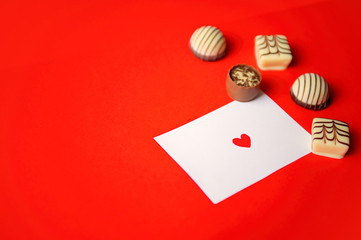 St. Valentine's Day. Chocolate candies and a note with a heart on red background. Chocolate candies. Chocolate treats. Assorted chocolates.