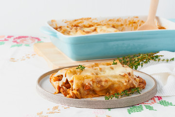 Cannelloni pasta with filling of ground beef, tomatoes, baked with bechamel tomato sauce and mozzarella. Classical Italian cuisine, white tablecloth with embroidery, rustic style, side view