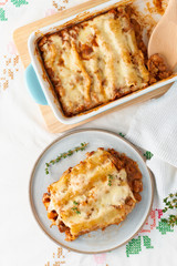 Cannelloni pasta with filling of ground beef, tomatoes, baked with bechamel tomato sauce and mozzarella. Classical Italian cuisine, white tablecloth with embroidery, rustic style, top view, vertical