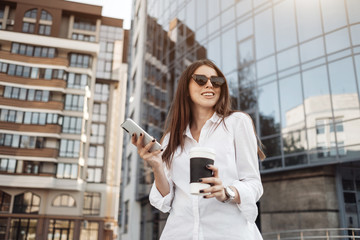 Portrait of One Fashionable Girl Dressed in Jeans and White Shirt Drinking Coffee and Using Her Smartphone, Business Lady, Woman Power Concept