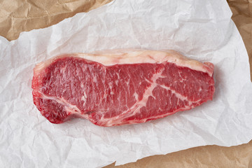 Big whole piece of raw beef meat, striploin on white parchment paper on craft background, zero...