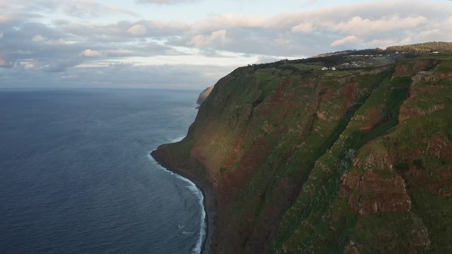 Aerial view of the lush green forest coastline. Flying above the ocean during an epic sunset. 