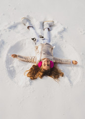 Snow angel made by a kid in the snow. Child girl playing and making a snow angel in the snow.