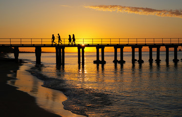People silhouetted at sunset on jetty at a Mornington Peninsula beach near Melbourne Australia.
